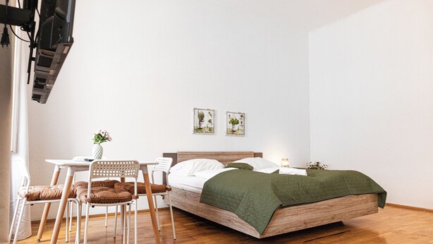 Un dormitorio con una cama de madera, ropa de cama blanca, una mesita con un florero y dos cuadros en la pared.