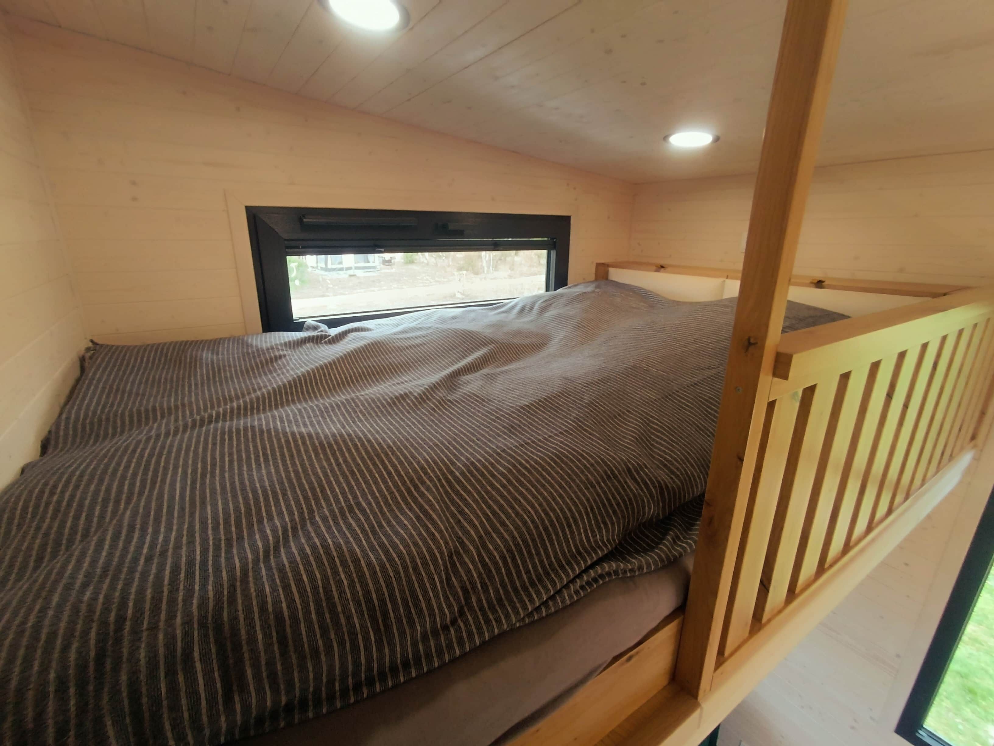 Una cama individual con colcha a rayas en una habitación con paredes de madera y una ventana.