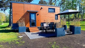 Eine moderne Holzhütte mit Tür, Fenstern und einer Terrasse mit Tischen und Stühlen.