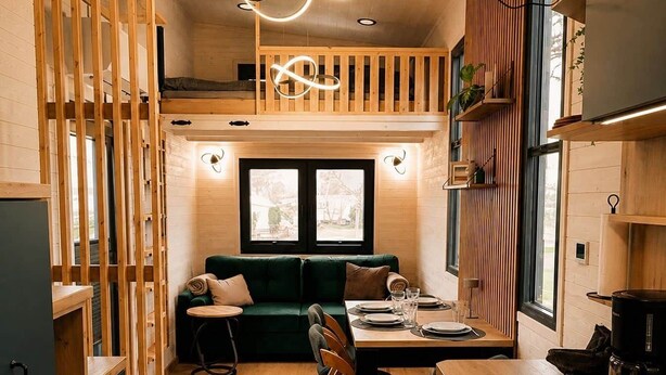Ein gemütliches Blockhauszimmer mit einem Holzesstisch, einem grünen Sofa und einer Küchenzeile inklusive Herd und Kaffeemaschine.