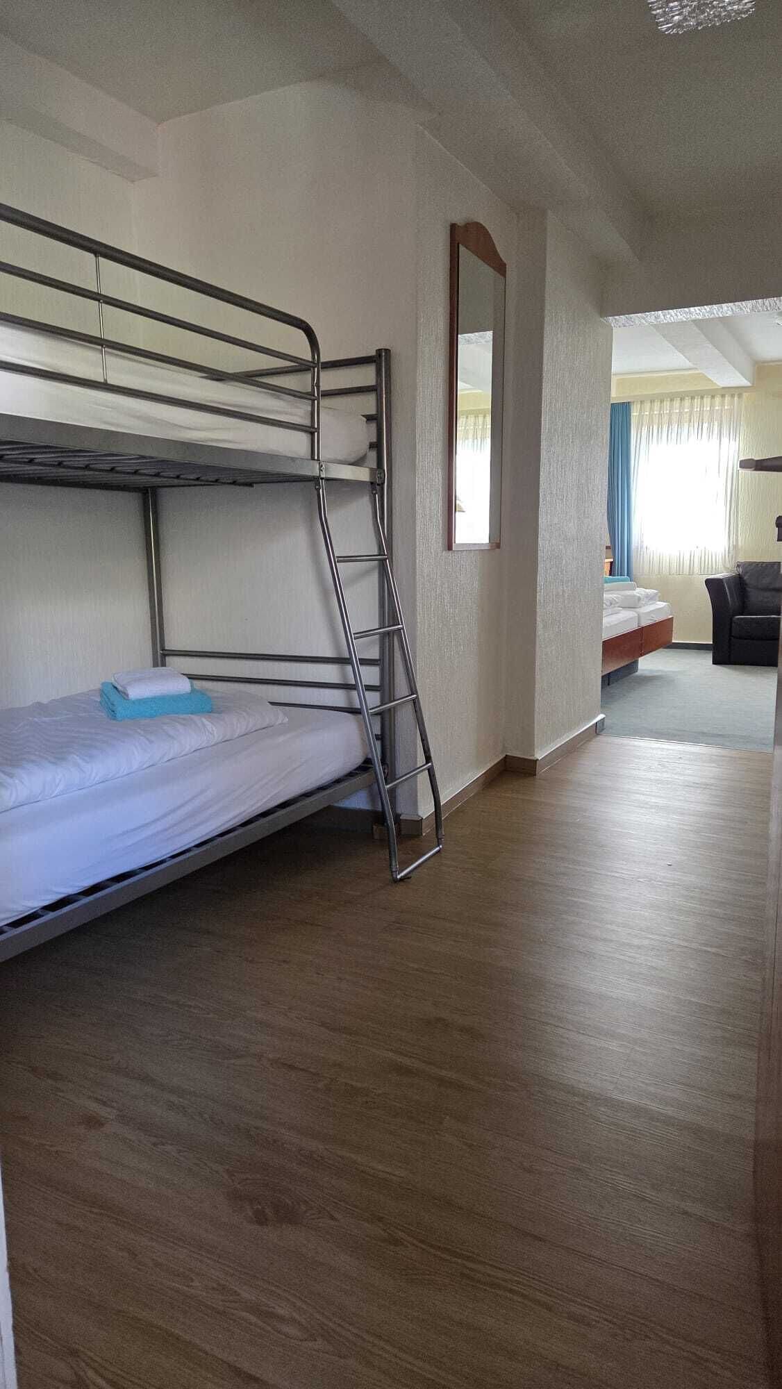 Ein Stockbett mit einer Leiter, einem kleinen Spiegel und einem Holzboden in einem Zimmer mit Balkonblick.