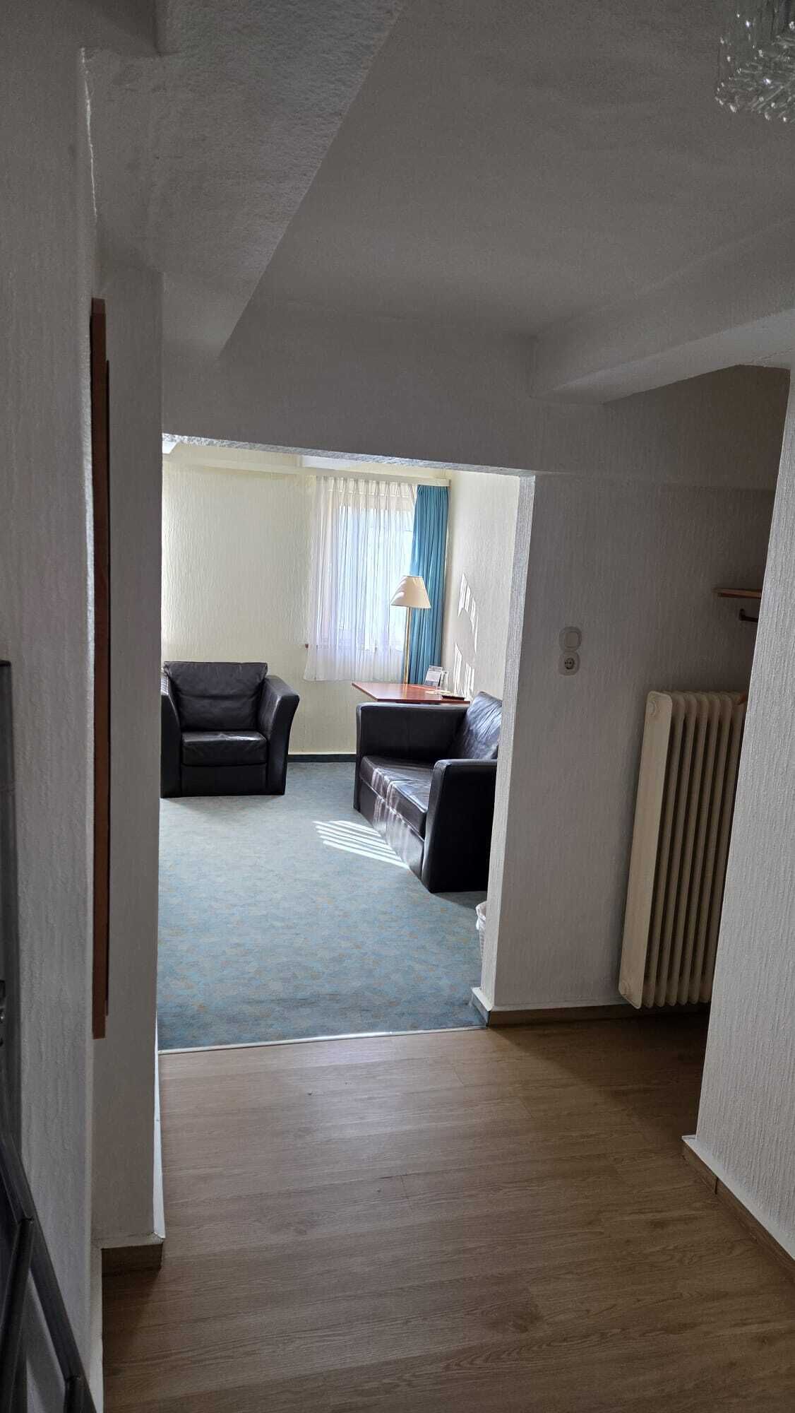 A room with a wooden floor, a radiator, and two black leather sofas.