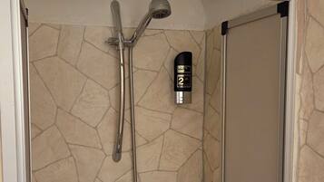 Aseo con mampara, pared con textura de piedra, ducha de mano y barra de ducha, además de un frasco de producto para el cuidado del vello corporal.