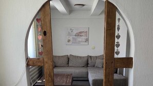 A room with a wooden-framed archway, a grey sofa, a small wooden table, and a blue towel on a bed.