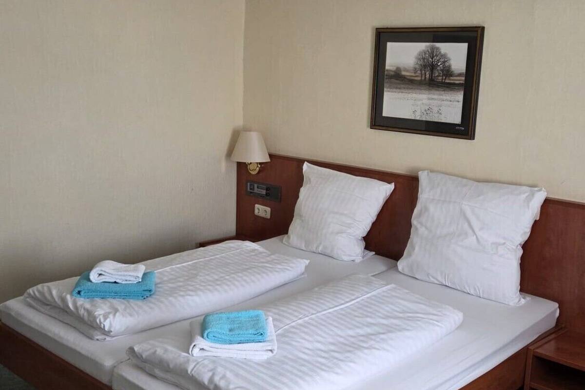 Een tweepersoonsbed met witte lakens, een houten hoofdbord, een nachtkastje met lamp en een lijst met foto aan de muur.