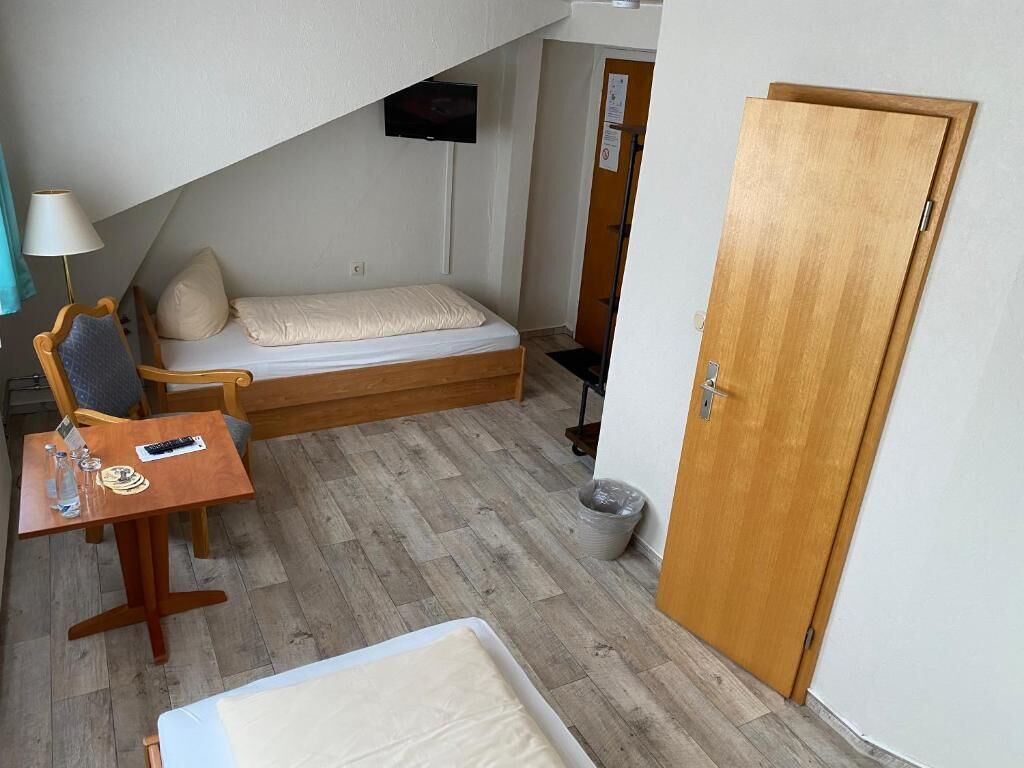 Een knus ogende kamer met een bed, een klein tafeltje met een lamp, een stoel en een aan de muur bevestigde televisie.
