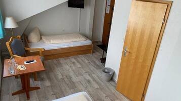 Een knus ogende kamer met een bed, een klein tafeltje met een lamp, een stoel en een aan de muur bevestigde televisie.