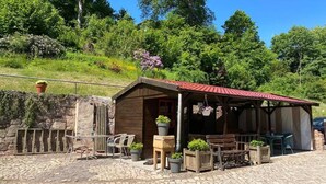 A rustic wooden building with a red-tiled roof, outdoor seating, and potted plants.