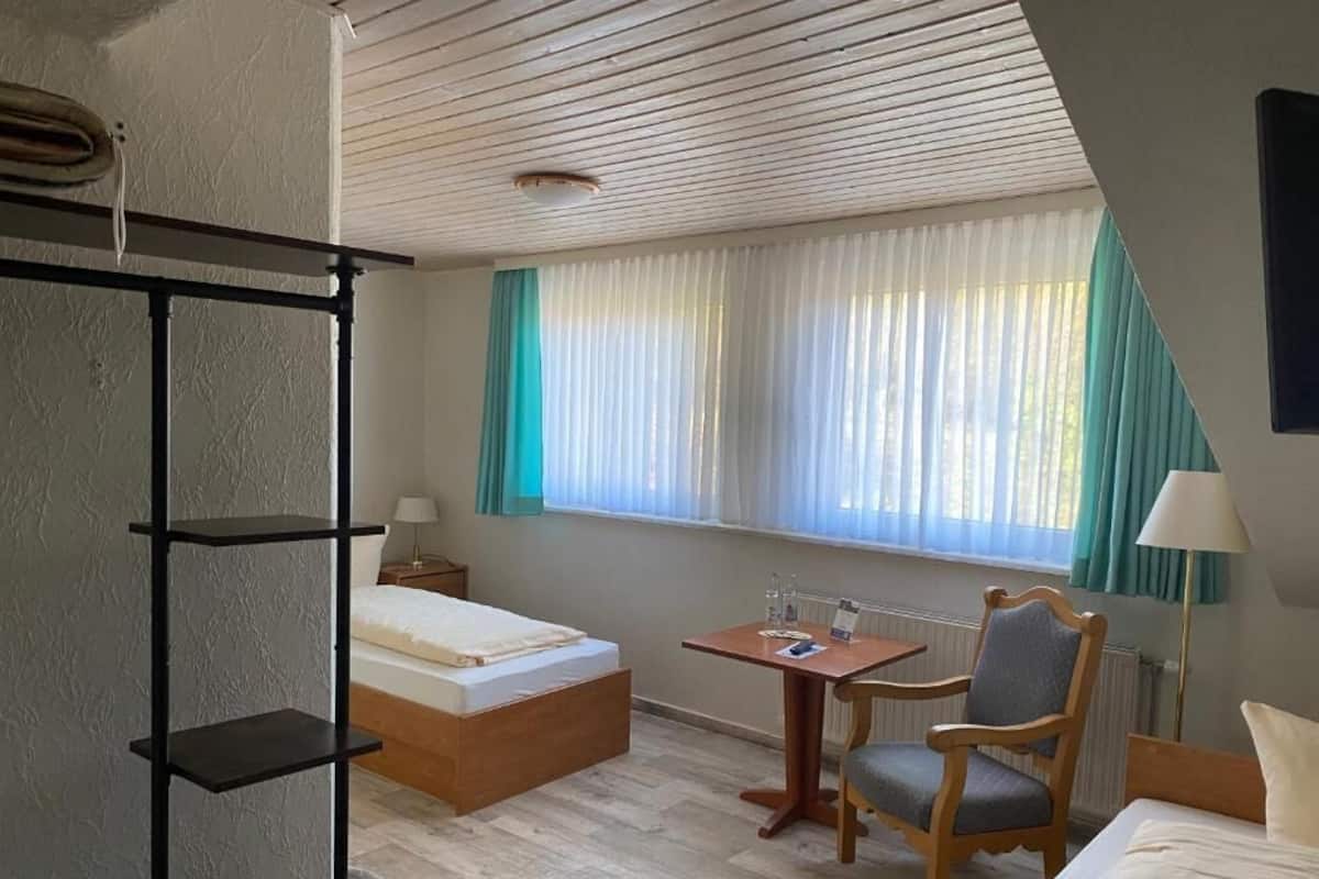 Een hotelkamer met een bed, een bureau, een stoel, een plank en een raam met gordijnen.