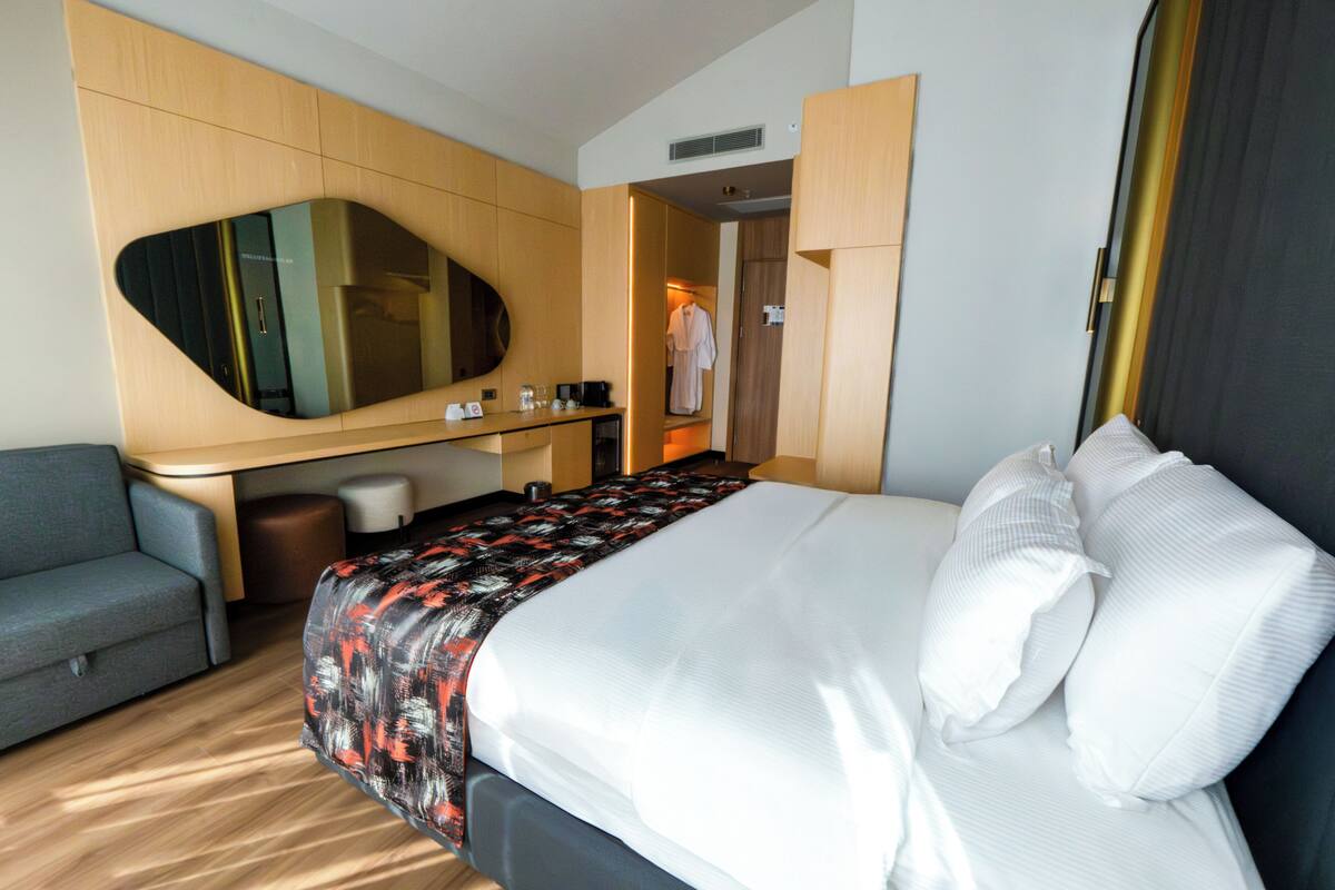 Et hotelværelse med seng, skrivebord, spejl, stol og garderobeskab.