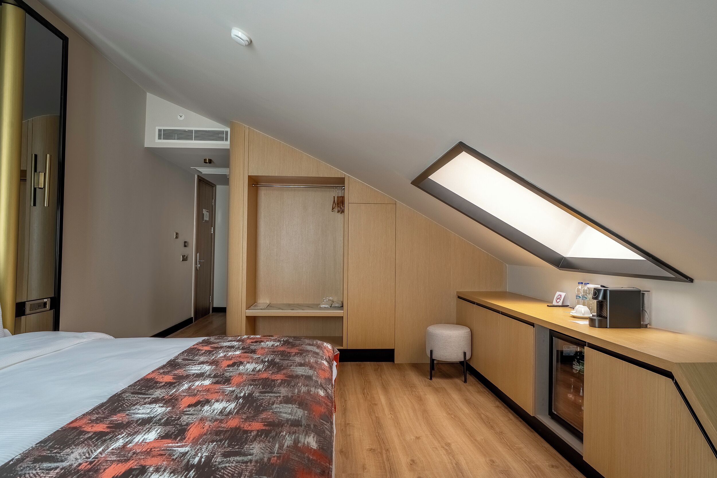 Habitación de hotel con cama, escritorio, silla, armario y unidad de aire acondicionado integrada.