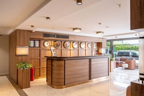 Un área de recepción moderna con un mostrador de madera, un reloj y una zona de estar con sofá y sillones.