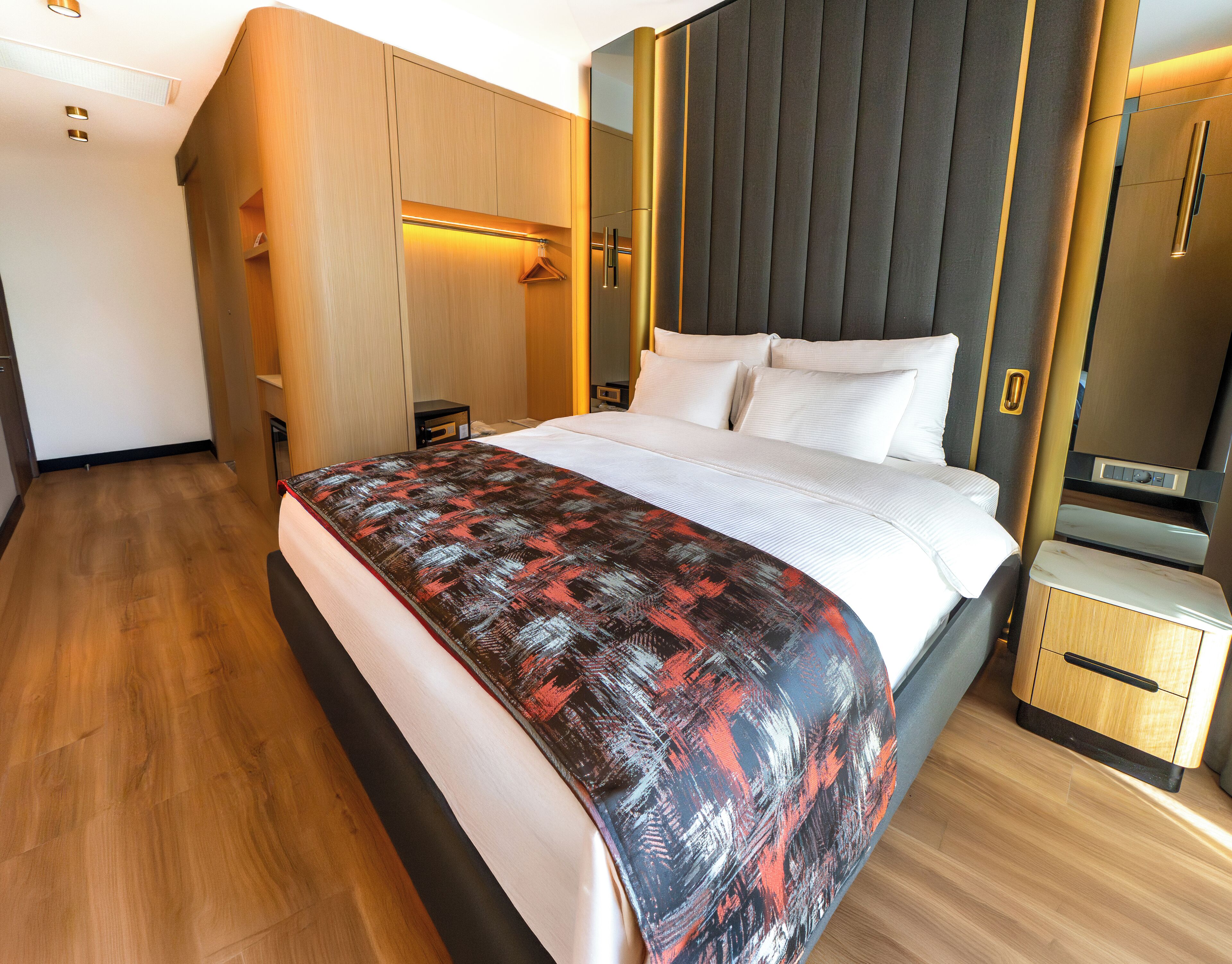 A modern hotel room with a large bed, built-in wardrobe, and a small bedside table.