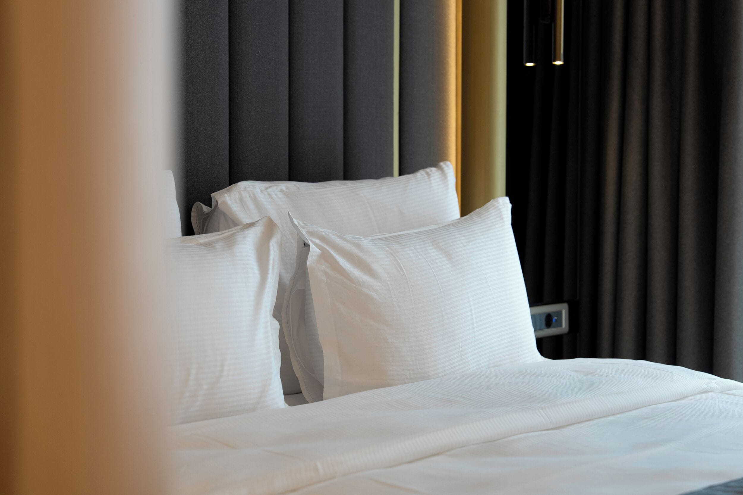 A neatly made bed with white linens, a dark headboard, and a wall-mounted control panel.