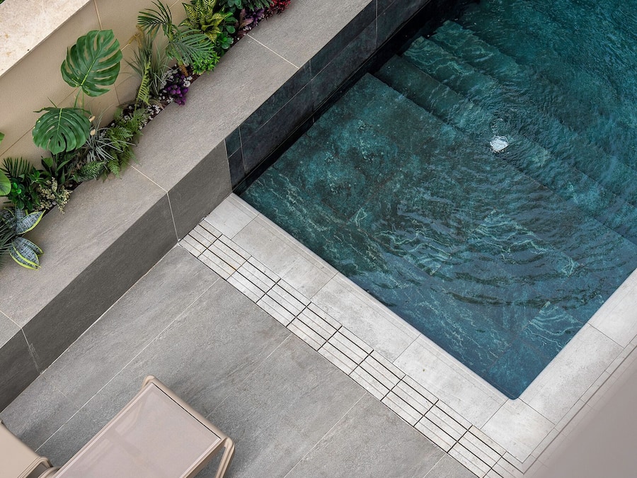 Une piscine à l’eau claire, entourée d’une terrasse carrelée et de chaises longues.
