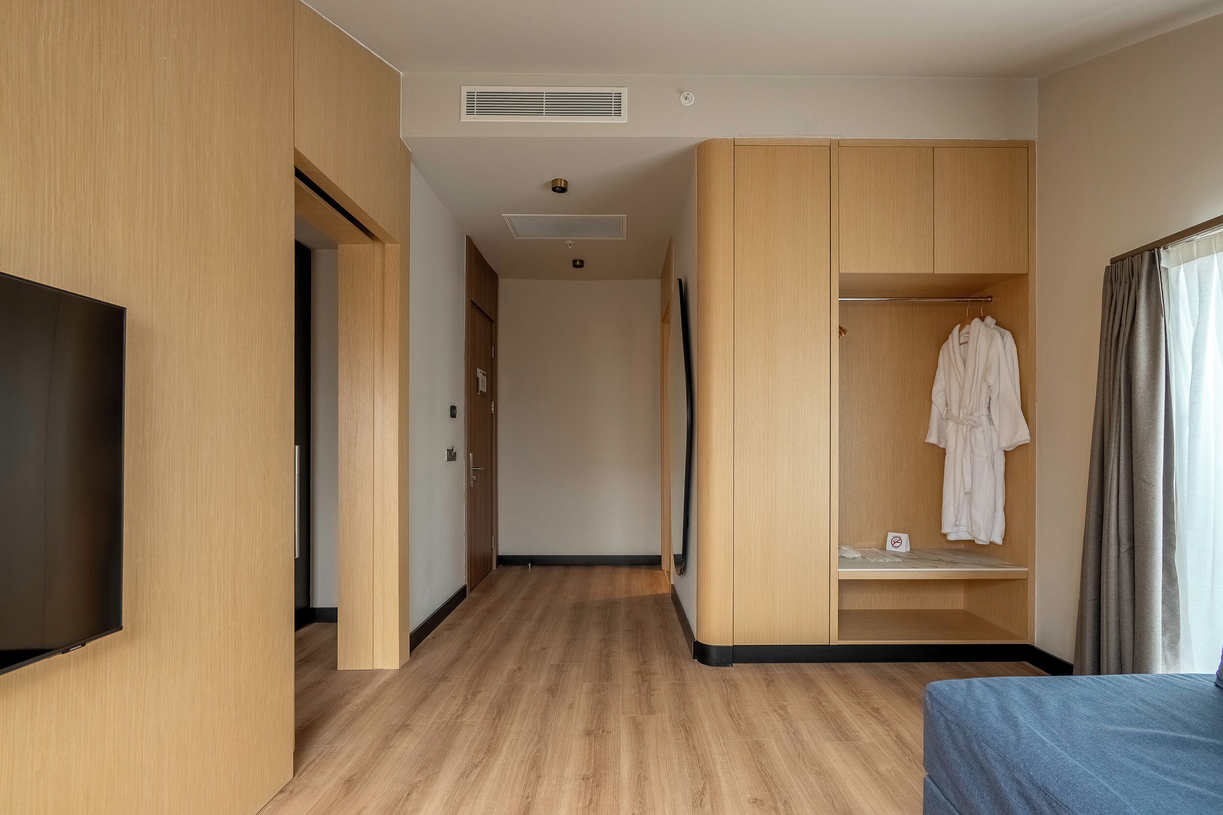 A hotel room with a TV, wooden wardrobe, a robe hanging, and a bed.