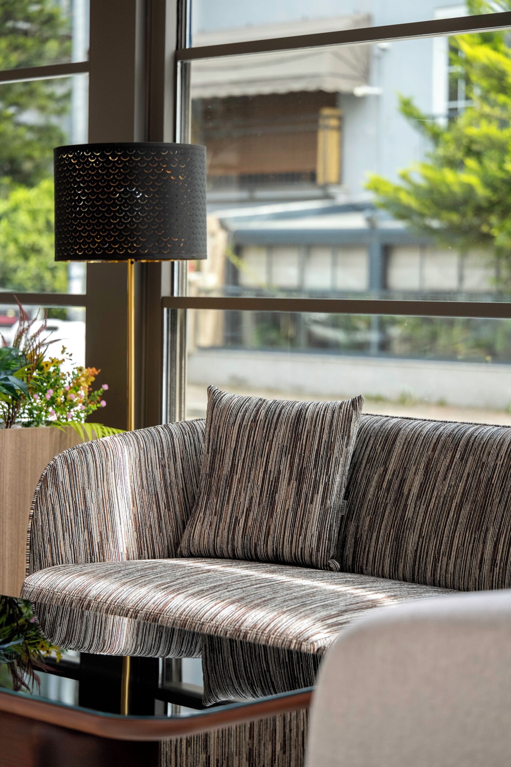Een moderne woonkamer met een bank, een vloerlamp en uitzicht door grote ramen.