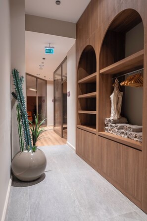 Un couloir avec une armoire en bois, une plante en pot et un panneau indiquant une sortie.