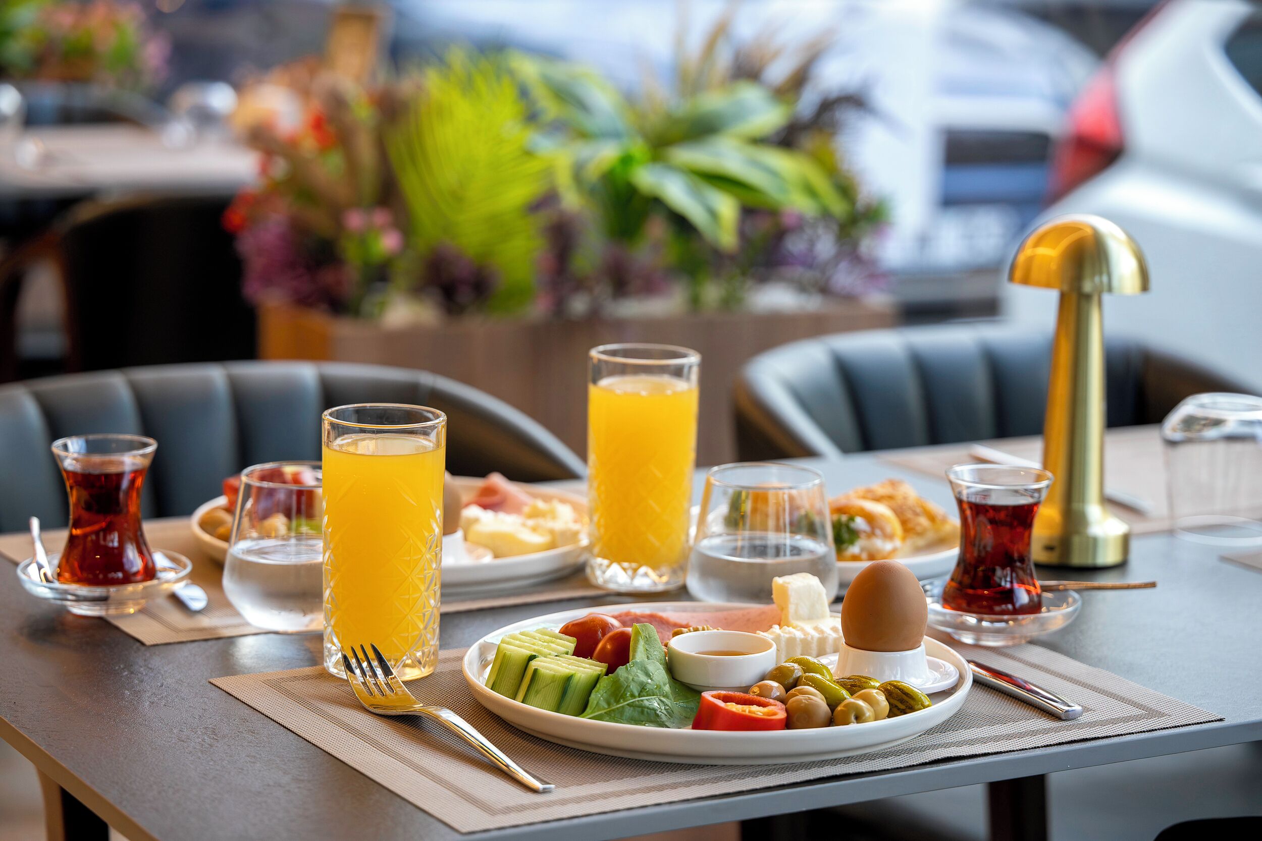 Une table de petit-déjeuner avec une assiette de nourriture, des verres de jus d’orange et une tasse de thé.