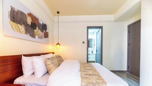 Een hotelkamer met een groot bed, een houten hoofdbord, wit beddengoed, een houten nachtkastje, een hanglamp en een schilderij aan de muur.