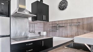 A modern kitchen with stainless steel appliances, a black cabinet, a clock, and a wooden backsplash. - Apartment 'Le Panorama' with Sea View, Balcony, Wi-Fi and Parking (Cassis)