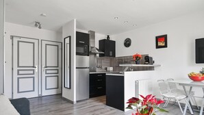 A modern kitchen with black cabinets, a stainless steel range hood, and a dining area with a white table and chairs. - Apartment 'Le Panorama' with Sea View, Balcony, Wi-Fi and Parking (Cassis)