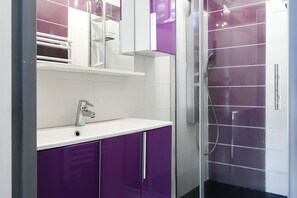A modern bathroom with a white sink, purple cabinets, a glass shower enclosure, and a mirror above the sink. - Apartment 'Le Panorama' with Sea View, Balcony, Wi-Fi and Parking (Cassis)