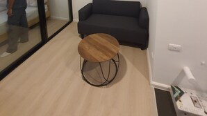 Een kamer met een donkerbruine bank, een ronde houten tafel, een grote spiegel en een bed met houten poten.
