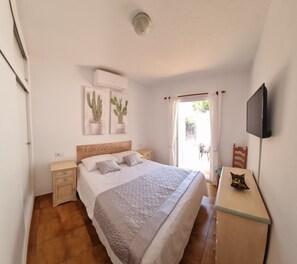 Une chambre à coucher avec un lit, des tables de chevet, un téléviseur et deux tableaux représentant des cactus.