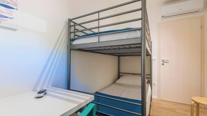 Ein Mehrbettzimmer mit Schreibtisch, Stuhl, einer Tür und einer Klimaanlage.