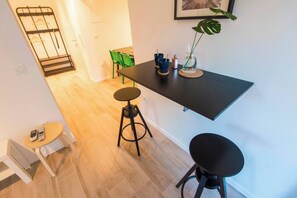 Une cuisine moderne avec un plan de travail noir, deux tabourets et un étagère suspendue.