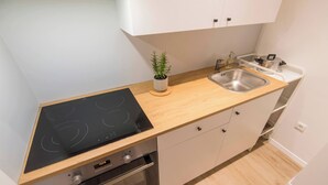 Eine kompakte Küche mit einem schwarzen Induktionskochfeld, einem Backofen, einer Spüle und einem kleinen Topfpflanzen.