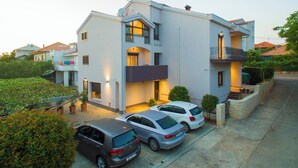 Ein modernes Wohnhaus mit zwei Etagen, einem Balkon und einer Garage, vor der drei Autos parken.