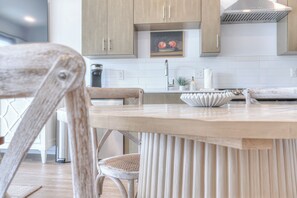 Een moderne keuken met houten kastjes, een witte betegelde achterwand en een ronde eettafel met een witte kom.