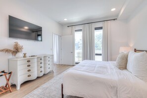 Een moderne slaapkamer met een groot bed, een witte dressoir, een flatscreen-televisie en uitzicht op de omgeving.