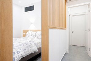 A bedroom with a bed, a bedside table, a wall-mounted light, a window, and a door. - Two Bedroom Deluxe Apartment (Siracusa)