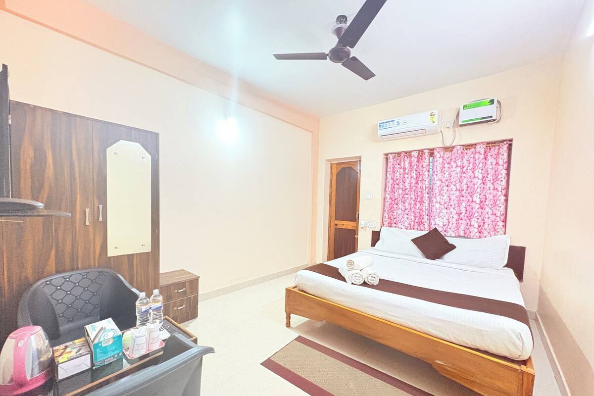 A hotel room with a bed, a desk with toiletries, a ceiling fan, and an air conditioning unit.