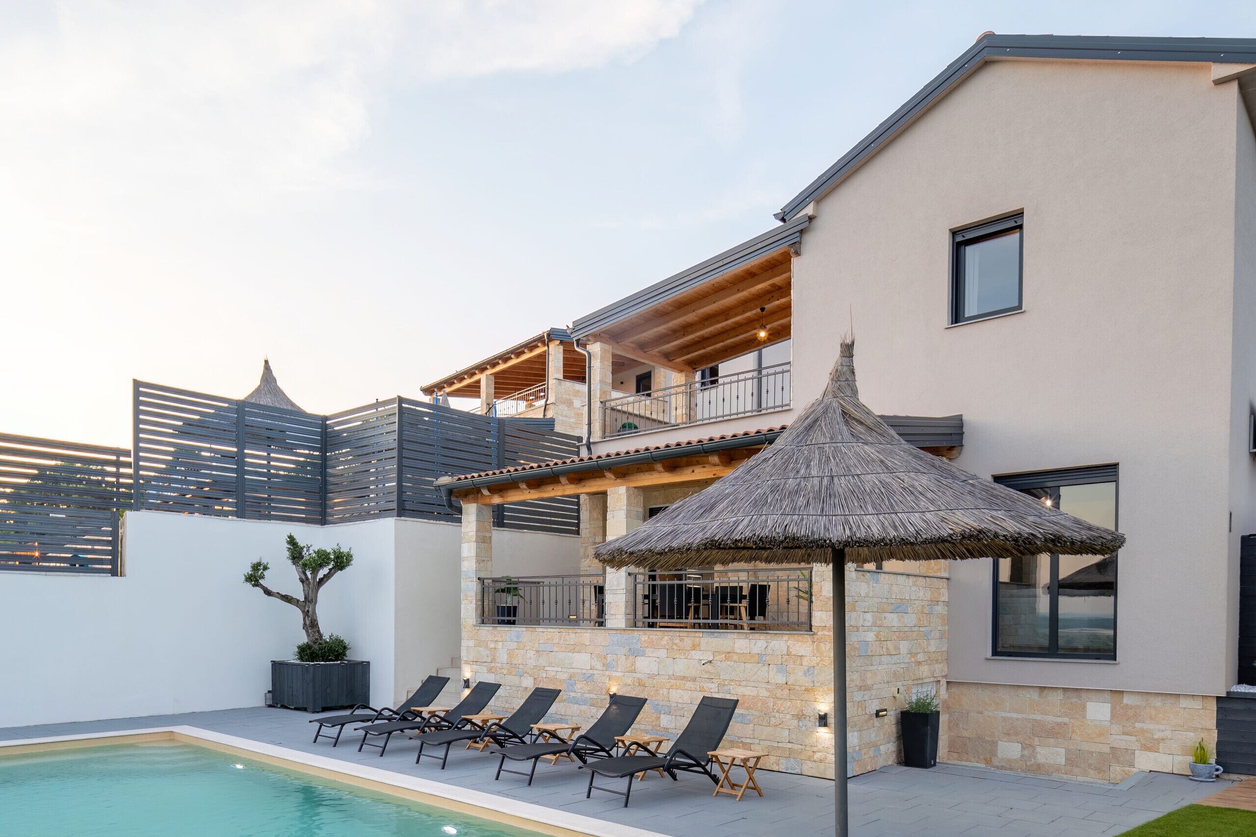 Um edifício moderno com piscina, espreguiçadeiras e uma estrutura de telhado de palha.