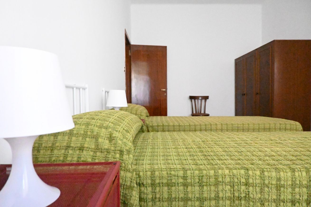 A room with two beds, a white lamp, a wooden wardrobe, and a small table.