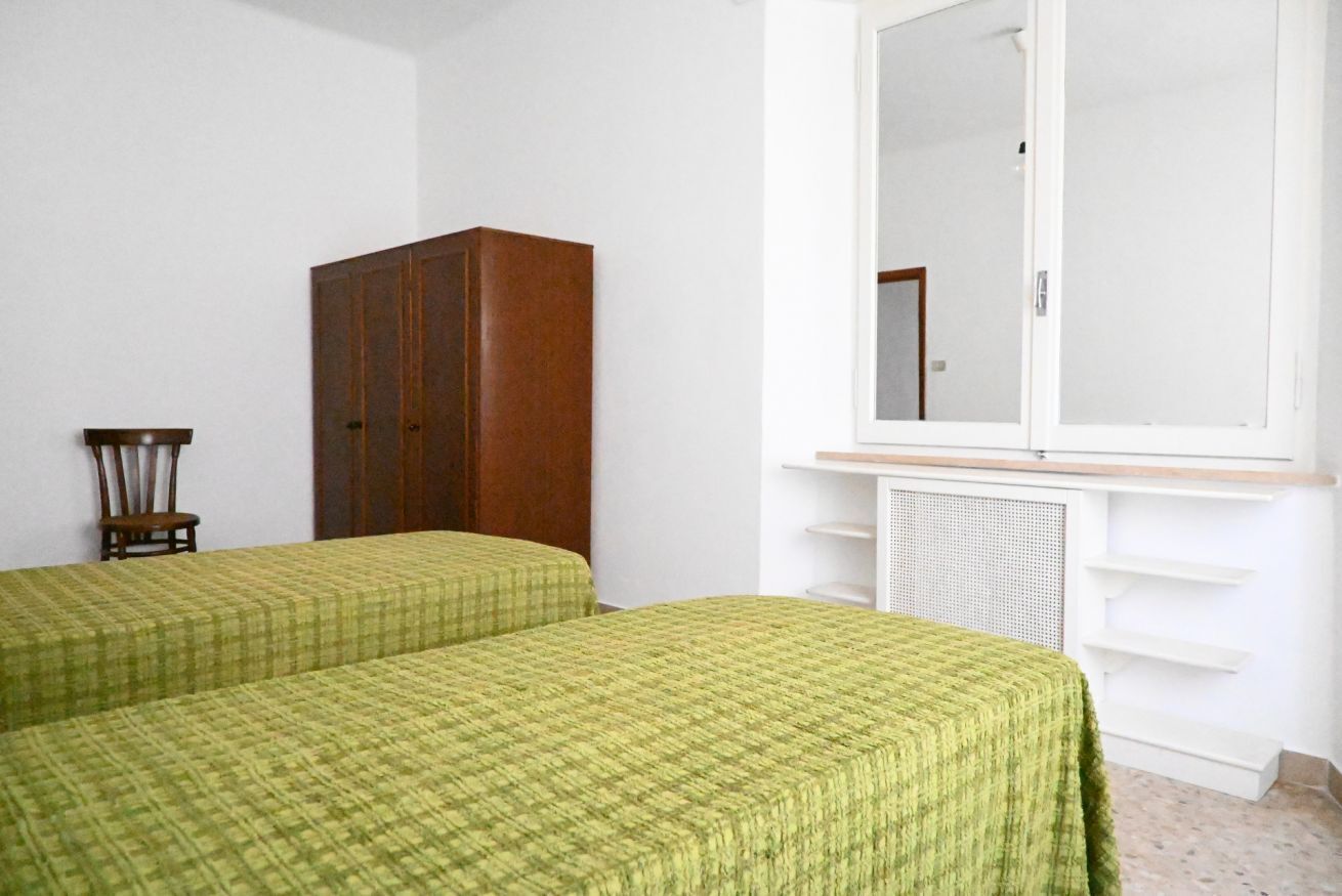 A room with two beds, a wooden wardrobe, a chair, and a large mirror above a radiator.