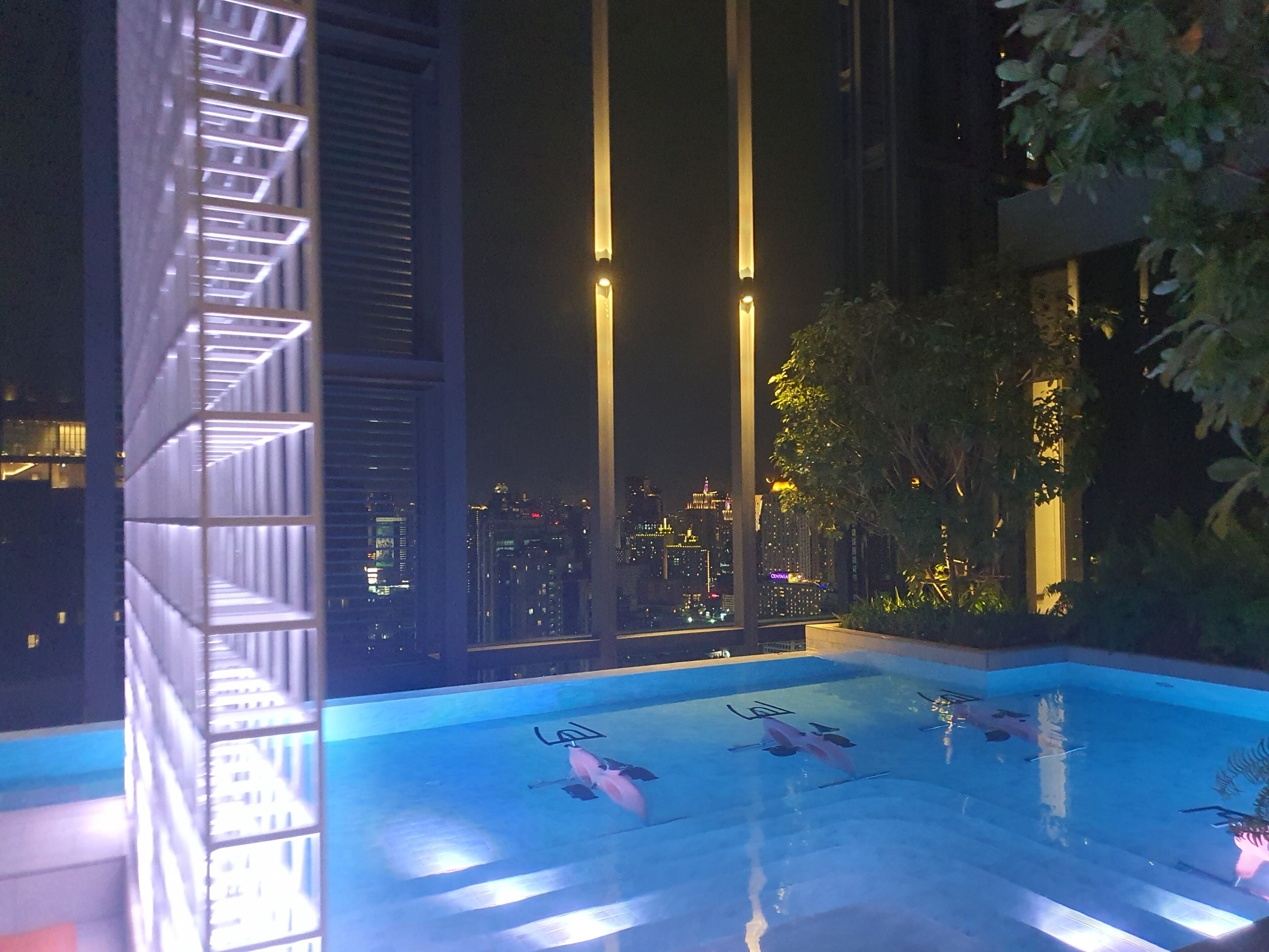 A nighttime view of a rooftop pool with a cityscape in the background.
