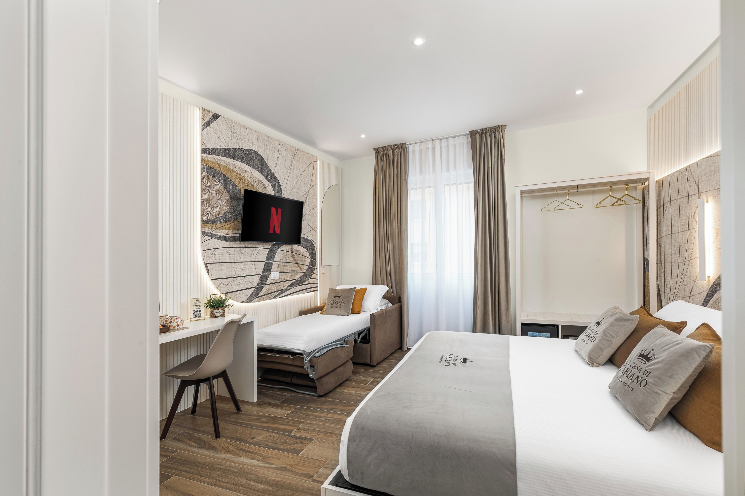 A hotel room with a bed, a desk, a TV, and a large mirror.