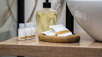 A bathroom vanity with a wooden bowl, a large white basin, and several toiletries including a bottle of lotion and a shower cap.