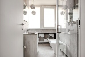 Ein modernes Badezimmer mit Duschkabine aus Glas, Toilette und Waschbecken, auf der Ablagefläche liegt ein Handtuch.