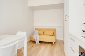 Ein Zimmer mit einem weißen Tisch, einem gelben Sofa und weißen Schränken.