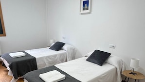 Et værelse med to enkeltsenge, hver med pude og et sammenfoldet håndklæde. Der er et lille bord med en lampe ved siden af sengen.