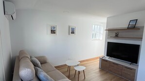 En moderne stue med en grå sofa, et lille hvidt bord og et fjernsyn på et træskab.