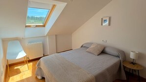 Een slaapkamer met dakraam, een bed, een stoel, een klein tafeltje en een radiator.