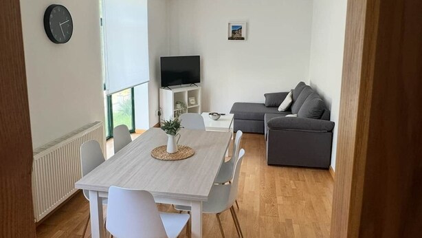 Een moderne woonkamer met een eethoek, een grijze bank, een flatscreen-tv en een klok aan de muur.