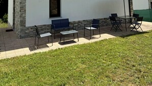 Un bâtiment à la façade en pierre, une enseigne indiquant « PORTOHOME 3 », des sièges extérieurs avec des chaises et une table, et un grand parasol.
